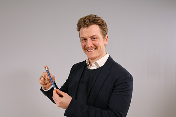 Linus Böll grinst in die Kamera und hält einem TROIKA Construction Multitasking Kugelschreiber in der Hand